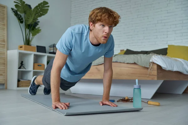 Confident Young Redhead Man Looking Concentrated While Exercising Home — Stockfoto