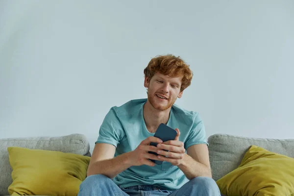 Allegro Uomo Rossa Utilizzando Smart Phone Mentre Rilassa Sul Divano — Foto Stock