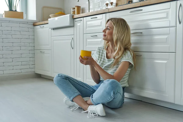 Beautiful Woman Holding Coffee Cup While Sitting Floor Leaning Kitchen — Foto de Stock