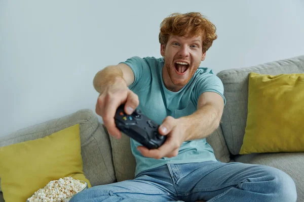 Alegre Pelirroja Hombre Usando Controlador Mientras Jugando Videojuegos Sofá Casa —  Fotos de Stock