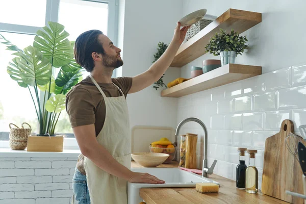Good Looking Young Man Placing Dishes Shelf While Standing Domestic — Foto Stock