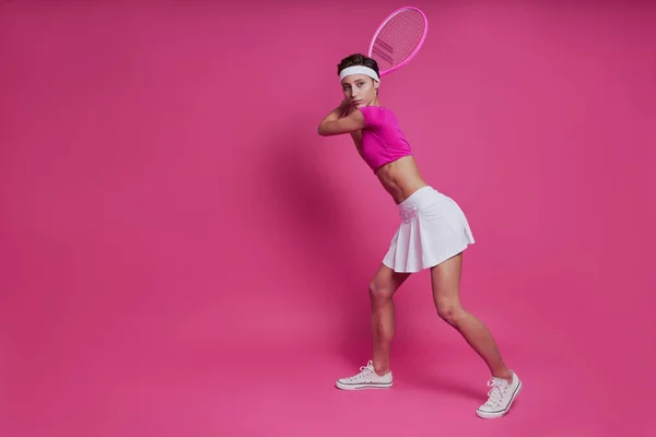 自信的年轻女子站在粉色背景下 手握网球拍 — 图库照片