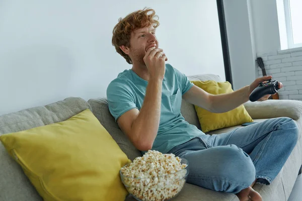 Happy Young Man Playing Video Games Enjoying Snacks While Sitting — Stock fotografie