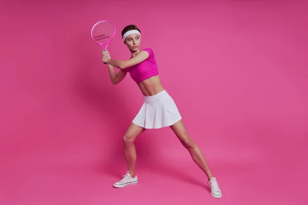 站在粉色背景下拿着网球拍的漂亮年轻女子 — 图库照片