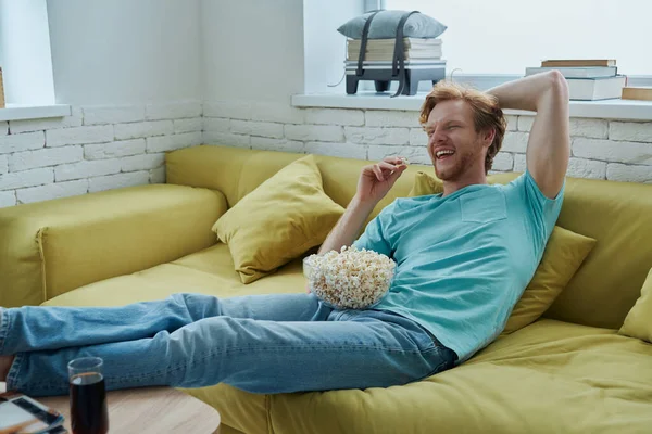 Happy Young Redhead Man Enjoying Snacks While Sitting Couch Home – stockfoto