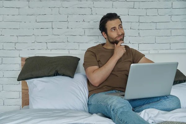 Продуманий Молодий Чоловік Використовує Ноутбук Сидячи Ліжку Вдома — стокове фото