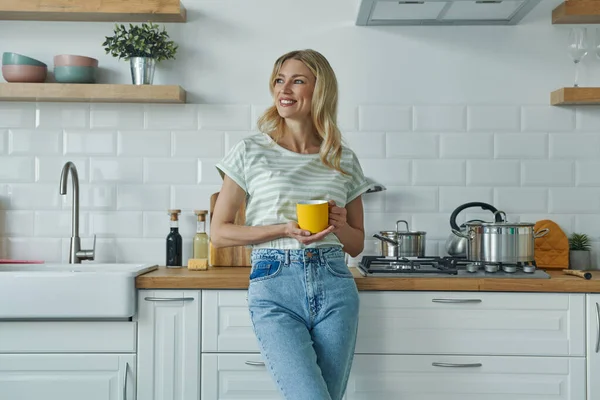 Cheerful Young Woman Holding Coffee Cup Leaning Kitchen Desk — Stock Fotó