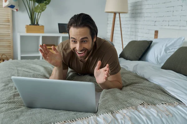 Surprised Young Man Working Laptop Smiling While Lying Bed Home — Stock fotografie