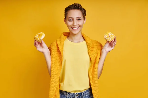 Счастливая Молодая Женщина Держит Два Пончика Стоя Желтом Фоне — стоковое фото