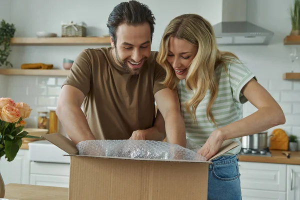 快乐的年轻夫妇站在厨房时打开包装盒 — 图库照片