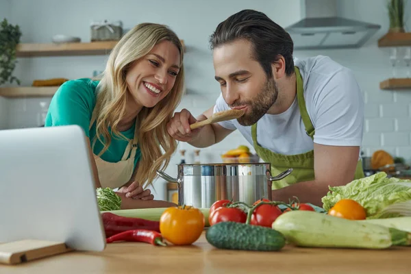 一对快乐的年轻夫妇在自家厨房的锅子里尝了点东西 — 图库照片
