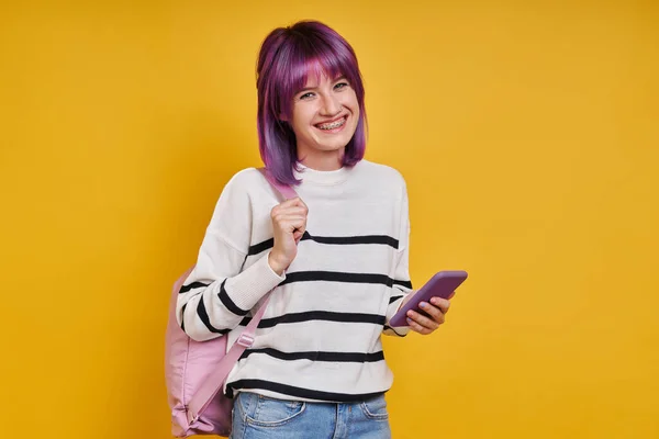 Szczęśliwa Nastolatka Plecakiem Trzyma Smartfon Stojąc Żółtym Tle — Zdjęcie stockowe