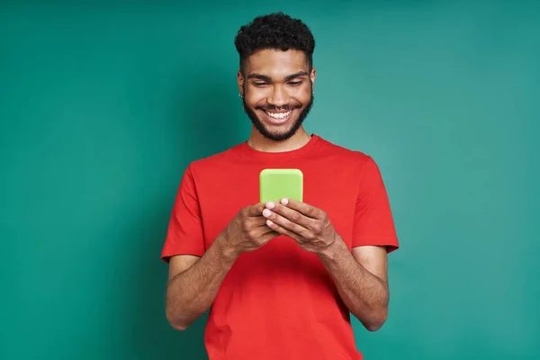 在绿色背景下 快乐的非洲男人一边用智能手机一边微笑 — 图库照片