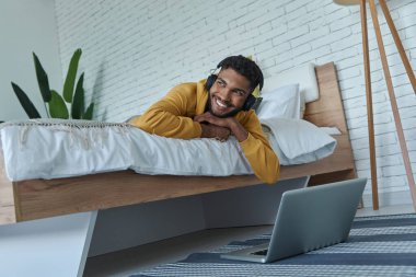 Dreamful African man in headphones relaxing on bed at home