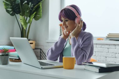 Concentrated young woman with purple hair using laptop while sitting at her working place