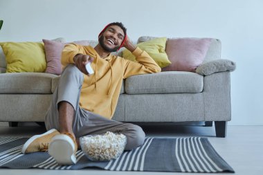 Rahatlamış genç Afrikalı adam evde yerde otururken televizyon seyrediyor ve gülümsüyor.