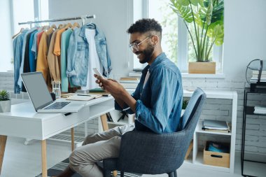 Moda mağazasında otururken akıllı telefon kullanan kendinden emin bir Afrikalı.