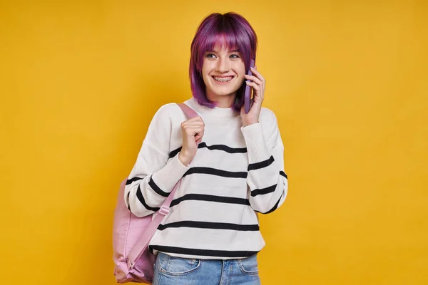 Cheerful Teenage Girl Backpack Talking Mobile Phone Yellow Background — Zdjęcie stockowe