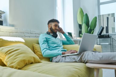 Handsome African man using laptop while sitting on the couch at home