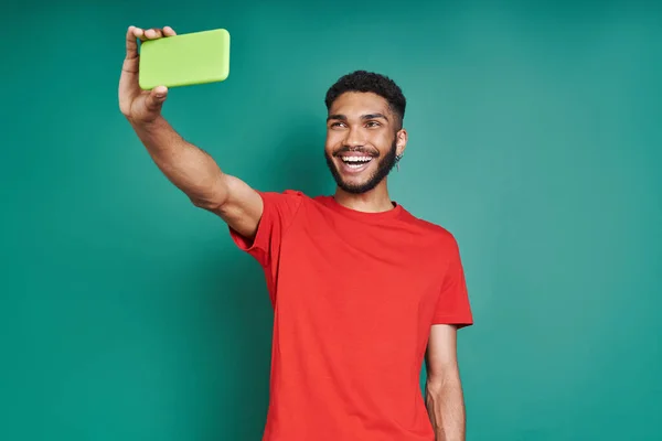 Happy African Człowiek Pomocą Smartfona Uśmiecha Się Stojąc Zielonym Tle — Zdjęcie stockowe