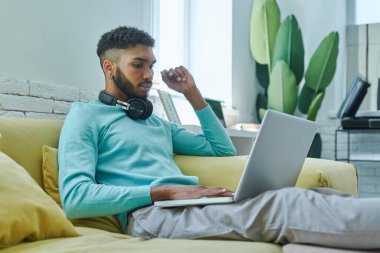 Evde kanepede otururken dizüstü bilgisayar kullanan kendinden emin bir Afrikalı.