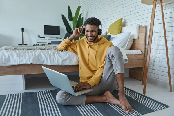 Cheerful African Man Headphones Using Laptop While Sitting Floor Bed — Foto Stock