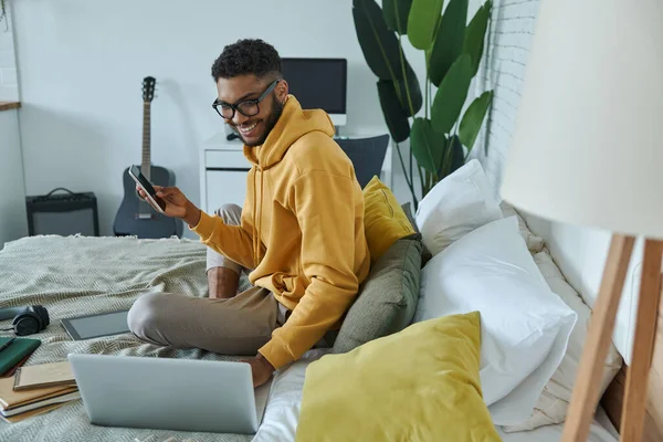 Cheerful African Man Using Technologies While Sitting Bed Home — 스톡 사진