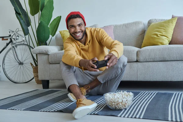 Χαρούμενος Νεαρός Αφρικανός Που Παίζει Βιντεοπαιχνίδια Ενώ Κάθεται Στο Πάτωμα — Φωτογραφία Αρχείου