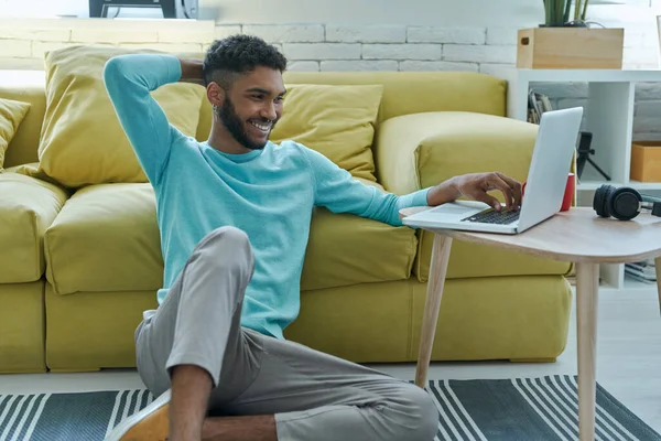 Relaxed African Man Using Laptop Smiling While Sitting Floor Home — Stockfoto