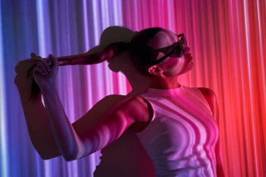 Gözlüklü çekici genç kadın renkli ışıklarla duvara yaslanıyor.