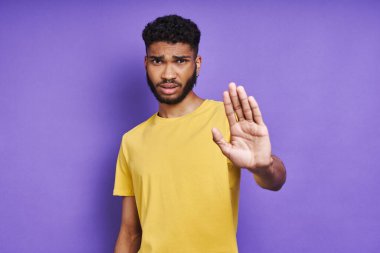 Genç Afrikalı bir adam mor arka planda dururken kolunu açık tutuyor.