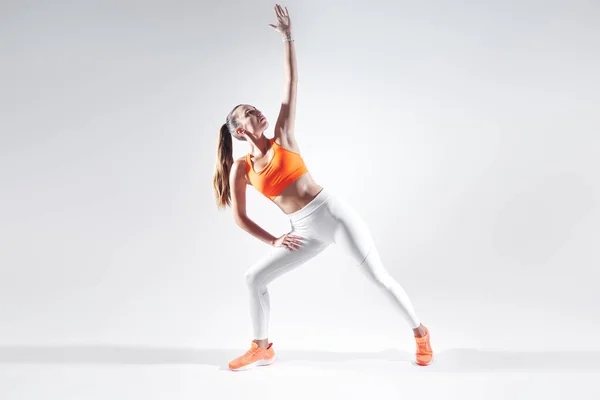 Beautiful young woman in sports clothing doing stretching exercises against white background