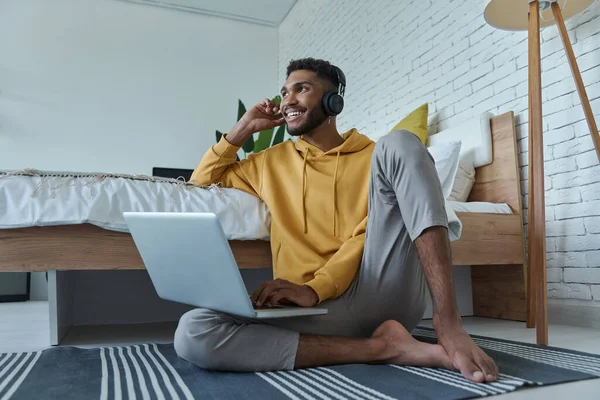 Cheerful African Man Headphones Using Laptop While Sitting Floor Bed — Stockfoto