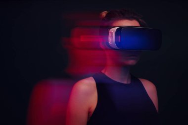 Karanlık arka planda sanal gerçeklik gözlüğü takan kendinden emin genç bir kadın.