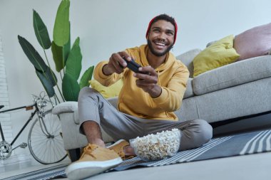 Mutlu genç Afrikalı adam evde yerde otururken video oyunu oynuyor.