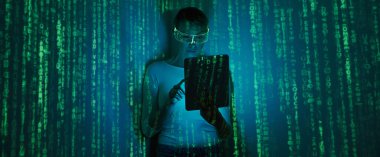 Confident woman in futuristic glasses using digital tablet against dark background with green symbols