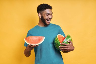 Karpuz tutan yakışıklı Afrikalı adam, sarı arka planda dururken gülümsüyor.