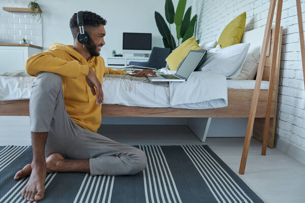 Счастливый африканский мужчина, проводящий веб-конференцию и жестикулирующий, лежа дома