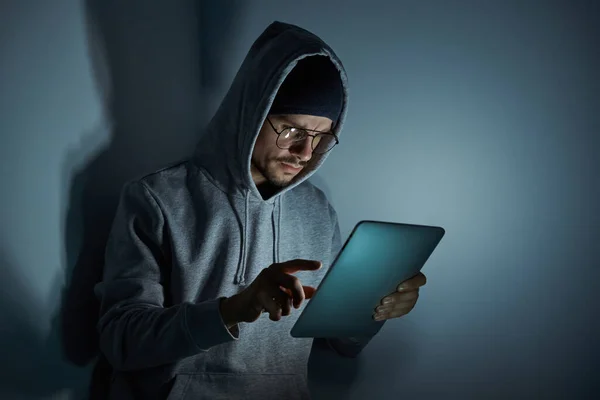 Confident young man in hooded shirt using digital tablet while working late