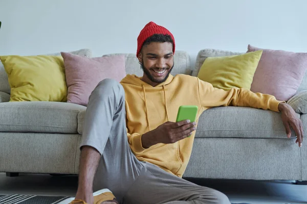 Cheerful Young African Man Using Smart Phone While Sitting Floor — Stock Photo, Image