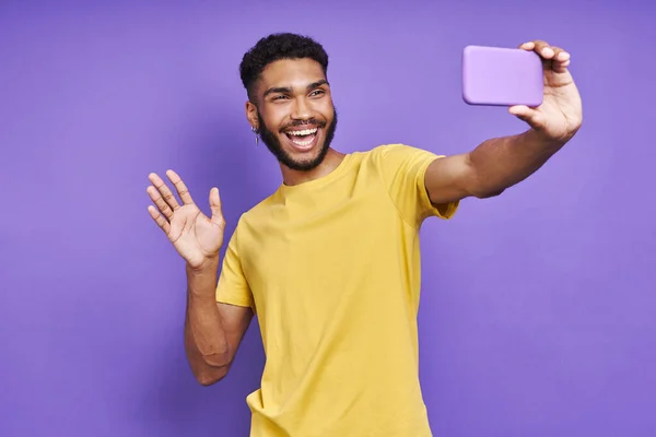 Playful African Man Looking Smart Phone Waving Hand Purple Background — Zdjęcie stockowe