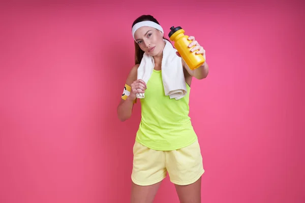 Pewna Siebie Kobieta Sportowej Odzieży Wyciągająca Rękę Butelką Różowym Tle — Zdjęcie stockowe