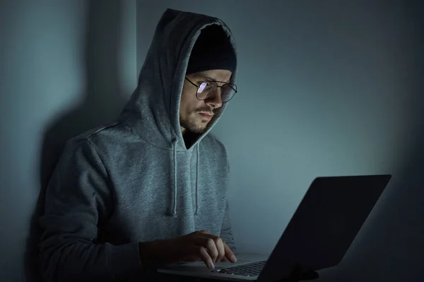 Confident young man in hooded shirt using computer while working late