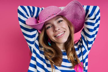 Renkli arka planda dururken pembe şapkalı güzel bir kadın başının arkasında el ele tutuşuyor.