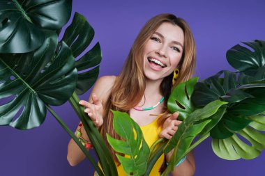 Çiçekten dışarı bakıp gülümseyen ve mor arka planda duran güzel bir genç kadın.