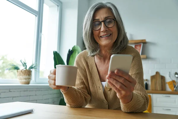 Mujer Mayor Alegre Disfrutando Bebida Caliente Uso Teléfono Inteligente Mientras — Foto de Stock