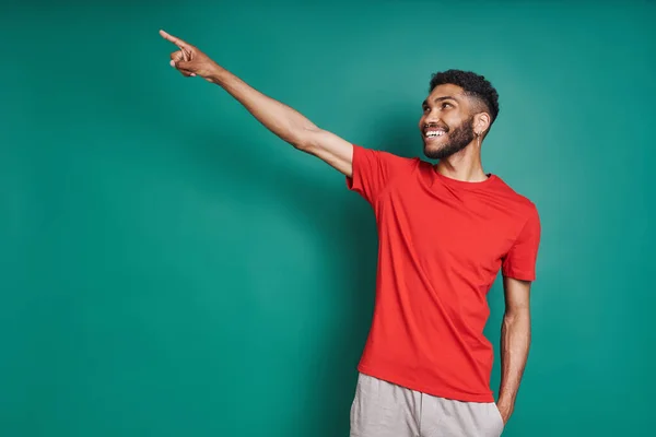 Handsome African man pointing away and smiling while standing against green background