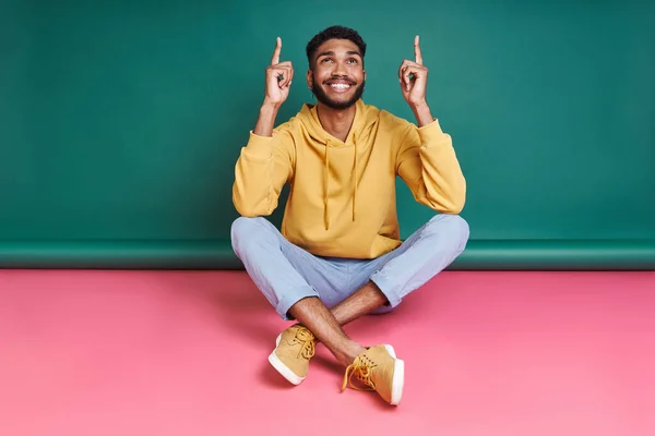 Cheerful African Man Pointing While Sitting Colorful Background — ストック写真
