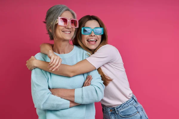 Filha Feliz Abraçando Sua Mãe Sênior Contra Fundo Rosa — Fotografia de Stock