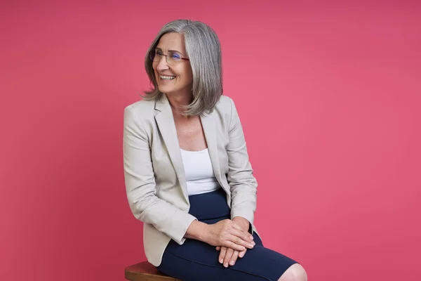Happy Senior Woman Formalwear Looking Away While Sitting Pink Background — Foto de Stock